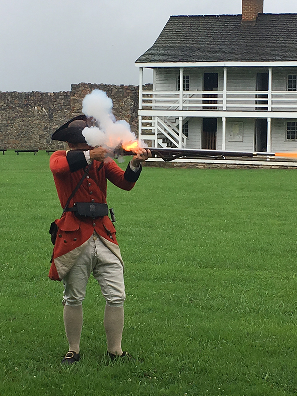 A person dressed as a solider and firing a musket.